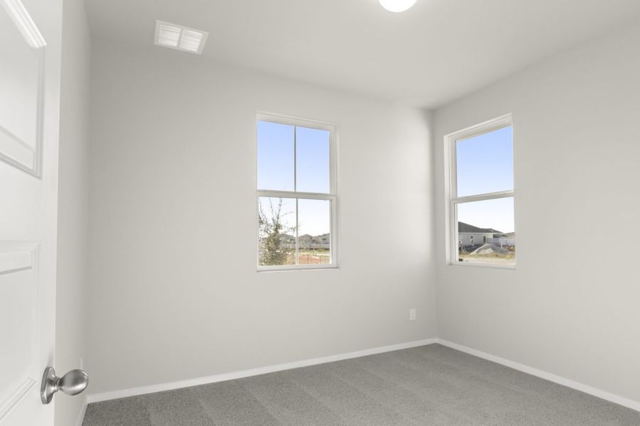 Image of a bedroom with tan carpeting and light grey walls with two windows