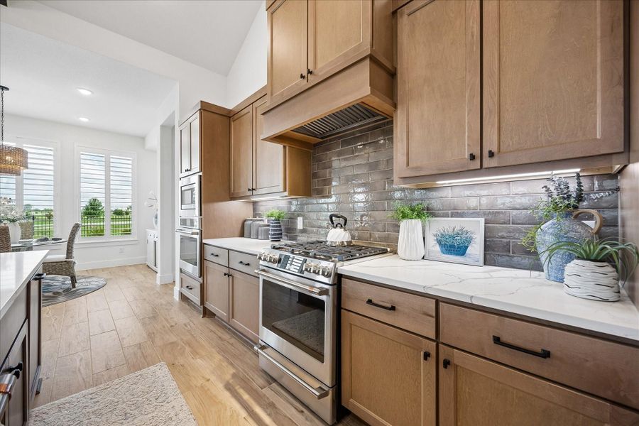 Beautifully appointed, the kitchen showcases a custom wood vent hood, an earthy-toned designer subway tile backsplash, and elegant under-cabinet lighting. Upgraded GE Café stainless steel appliances complement the space, while overlooking the backyard's scenic views.