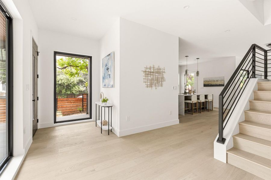 Open-concept entryway featuring light wood-finish flooring and a contemporary staircase with a black metal railing