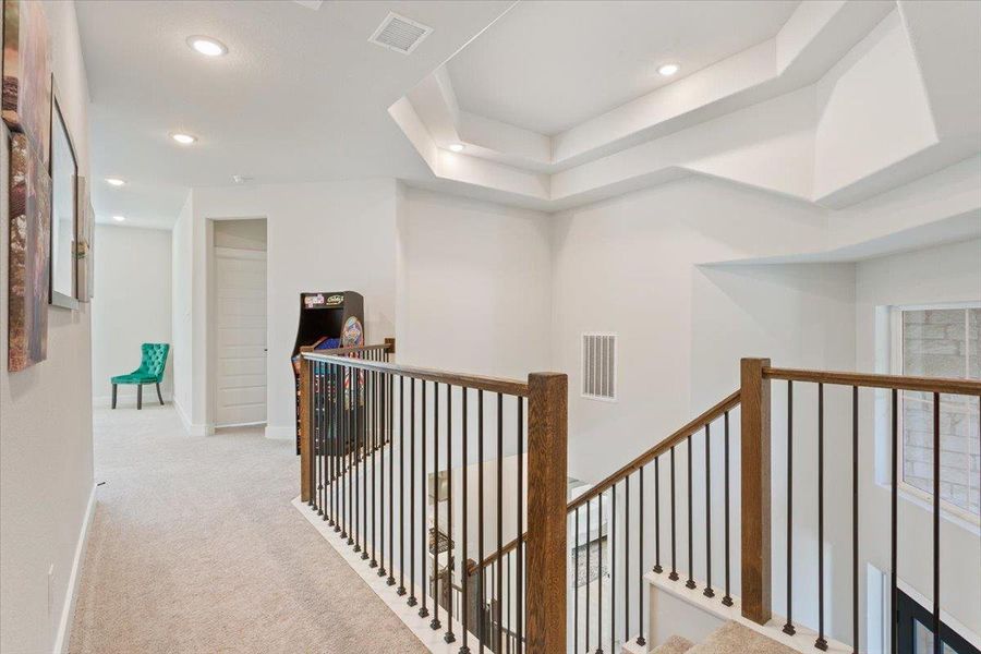 Corridor featuring light colored carpet, recessed lighting, a tray ceiling, and an upstairs landing