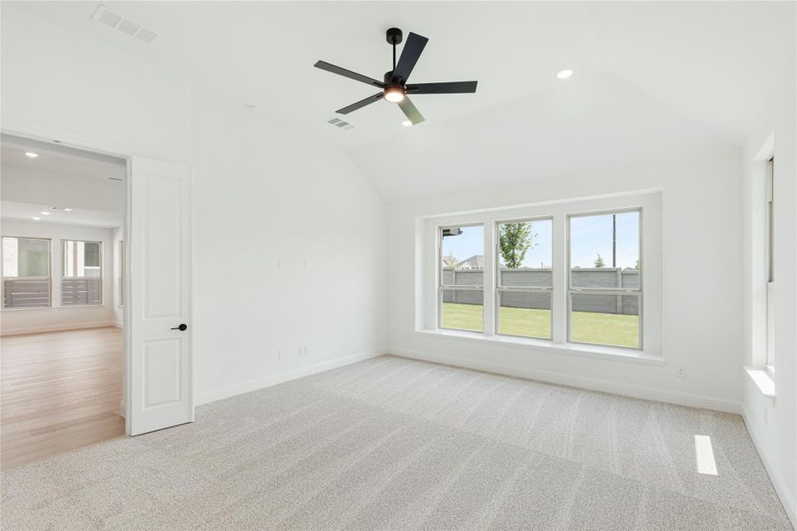 Empty bedroom with vaulted ceiling, ceiling fan, carpet flooring, and large windows overlooking backyard Empty bedroom with vaulted ceiling, ceiling fan, carpet flooring, and large windows overlooking backyard