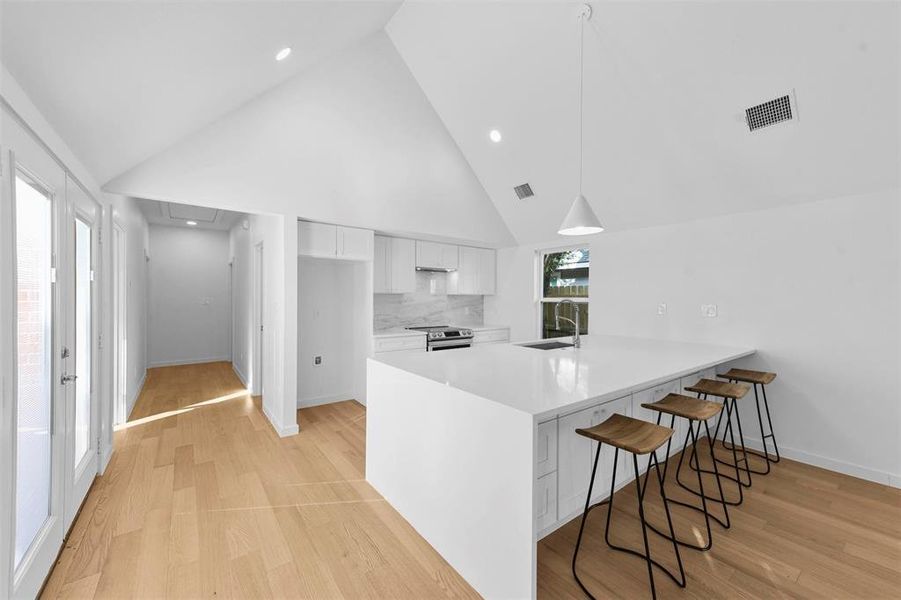 Kitchen with sink, kitchen peninsula, hanging light fixtures, white cabinets, and stainless steel electric range