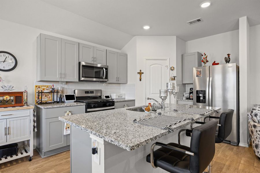 Kitchen with gray cabinetry, stainless steel appliances, backsplash, light stone counters, and light wood finished floors