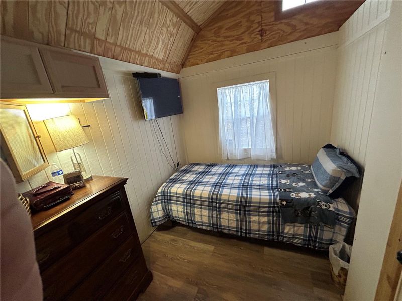 Bedroom featuring wood walls, dark wood finished floors, and lofted ceiling
