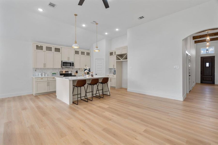 Kitchen featuring a breakfast bar, tasteful backsplash, glass insert cabinets, a kitchen island with sink, and light wood-type flooring