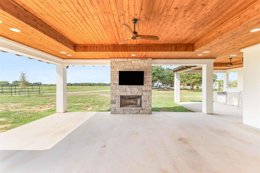 View of patio with an outdoor stone fireplace, exterior kitchen, ceiling fan, and a view of countryside View of patio with an outdoor stone fireplace, exterior kitchen, ceiling fan, and a view of countryside