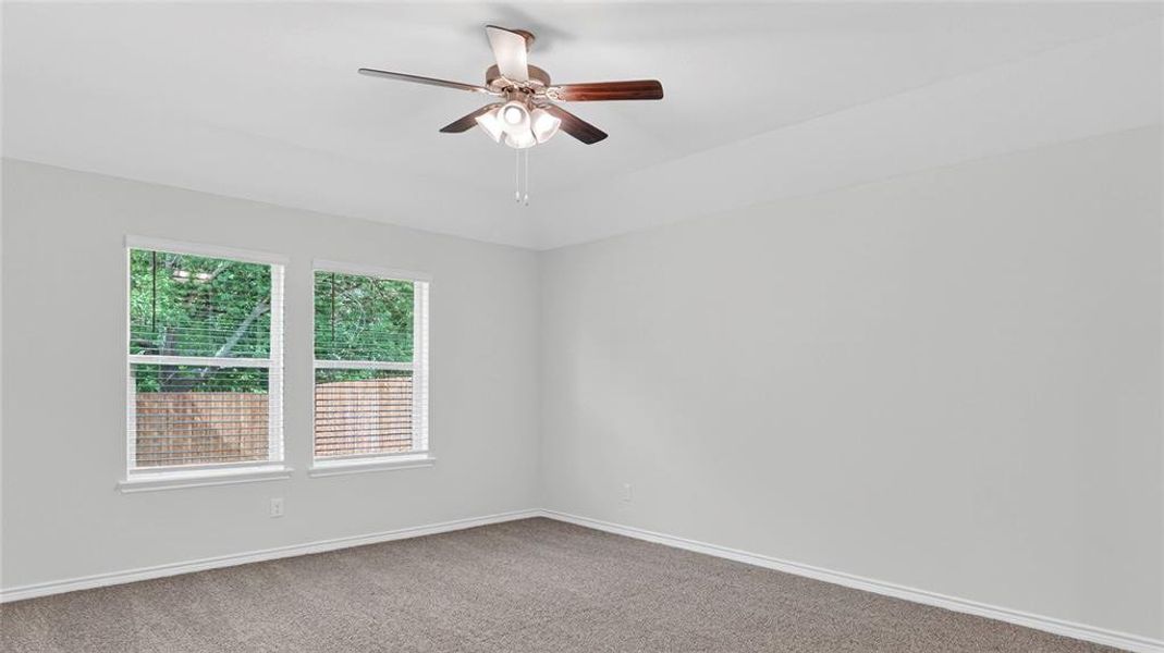 Spacious room featuring neutral carpet flooring, light gray wall paint, two white-framed windows with blinds, white baseboards, and a ceiling fan with integrated lighting