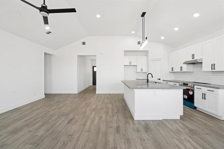 This is a bright, modern kitchen featuring white cabinetry, stainless steel appliances, a large center island, and wood-look flooring, all complemented by high ceilings with recessed lighting and a contemporary ceiling fan.