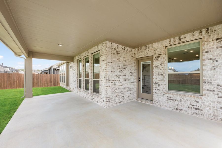 Covered back patio with concrete floor, light brick exterior, and fenced backyard with green lawn