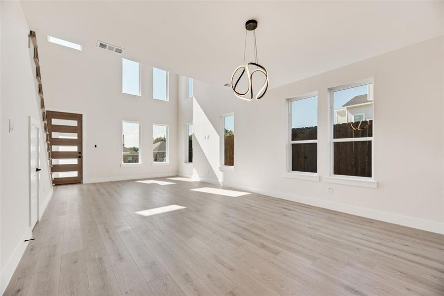 Unfurnished dining area featuring plenty of natural light, light wood-type flooring, a chandelier, and a towering ceiling Unfurnished dining area featuring plenty of natural light, light wood-type flooring, a chandelier, and a towering ceiling
