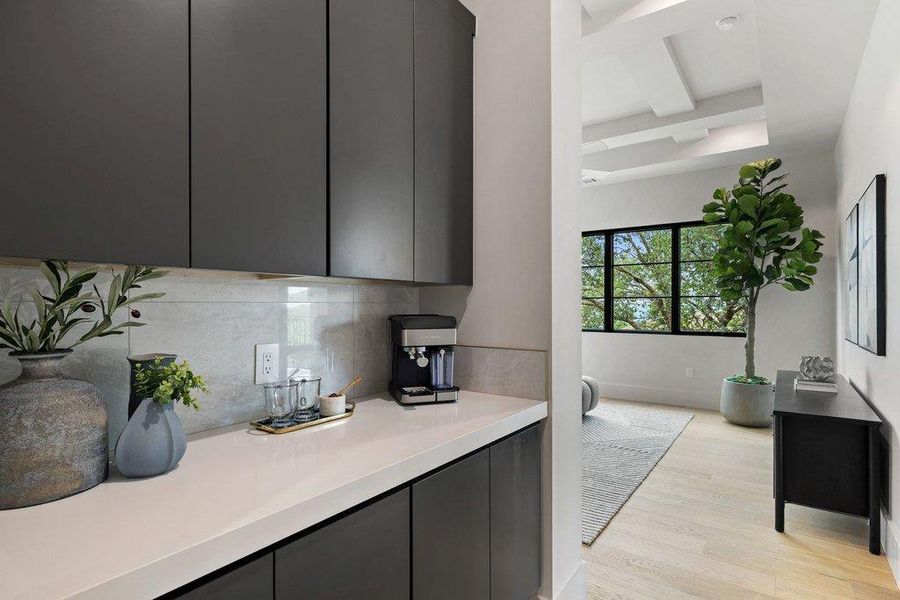 Built-in coffee bar featuring dark flat-panel cabinetry, a light countertop, and a tiled backsplash