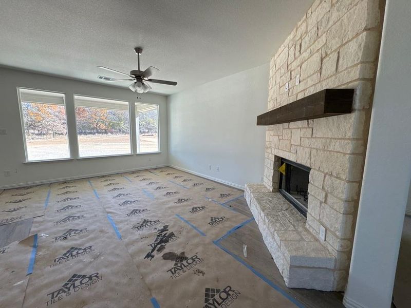 Unfurnished living room featuring a stone fireplace, a textured ceiling, and a ceiling fan