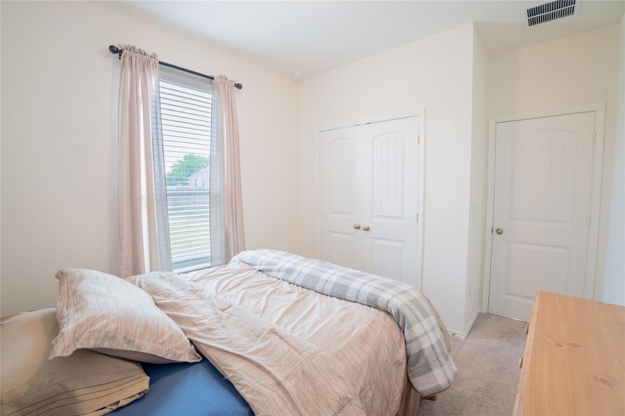 Bedroom featuring a double window with blinds, carpet flooring, a two-panel door, and a built-in closet with double doors Bedroom featuring a double window with blinds, carpet flooring, a two-panel door, and a built-in closet with double doors