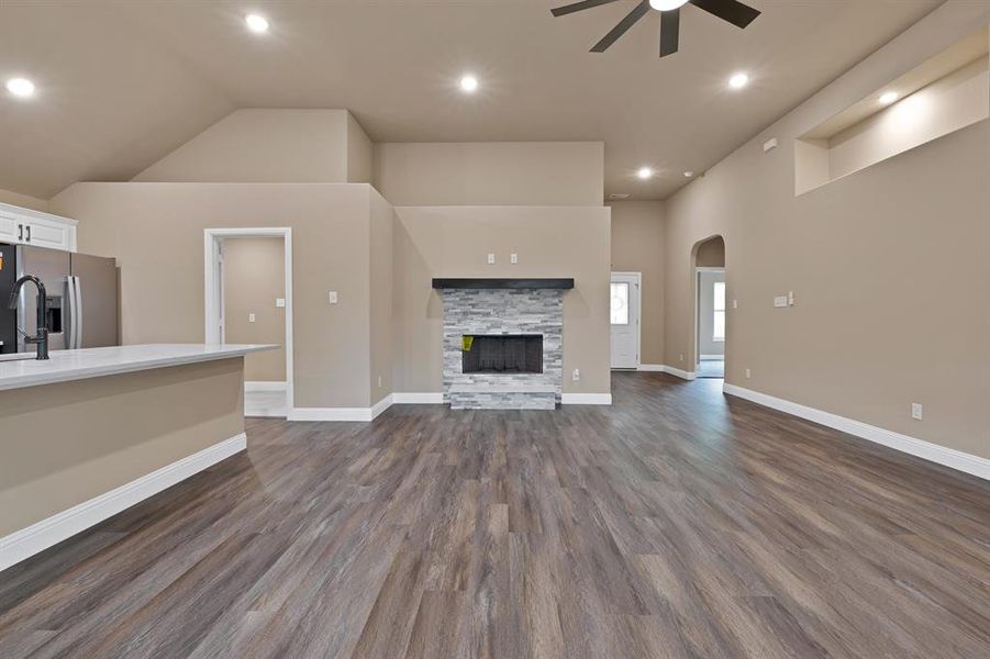 Unfurnished living room featuring dark wood-style floors, arched walkways, high vaulted ceiling, ceiling fan, and a fireplace Unfurnished living room featuring dark wood-style floors, arched walkways, high vaulted ceiling, ceiling fan, and a fireplace