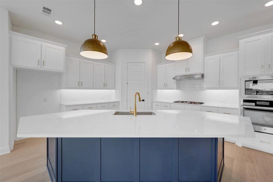 Dual tone kitchen featuring dual tone cabinets, a center island with sink, light stone counters, pendant lighting, and backsplash