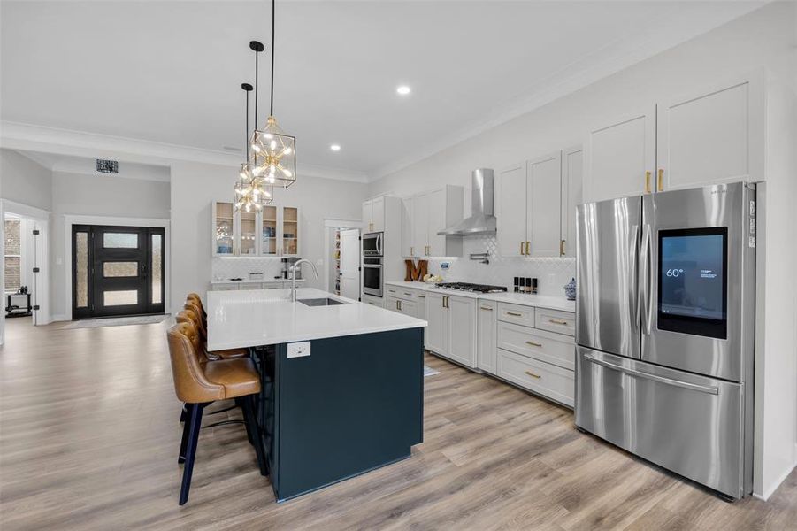 Kitchen featuring a kitchen bar, appliances with stainless steel finishes, wall chimney range hood, a center island with sink, and white cabinetry