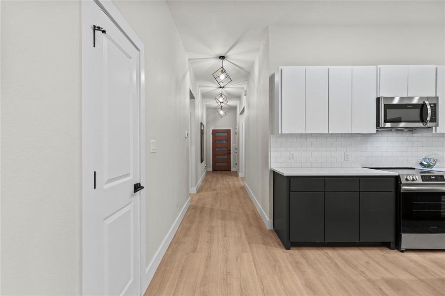 Kitchen with backsplash, white cabinets, stainless steel appliances, and light hardwood / wood-style floors