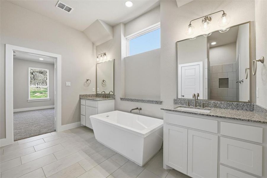 Bathroom with healthy amount of natural light, a freestanding bath, two vanities, light tile patterned floors, and recessed lighting