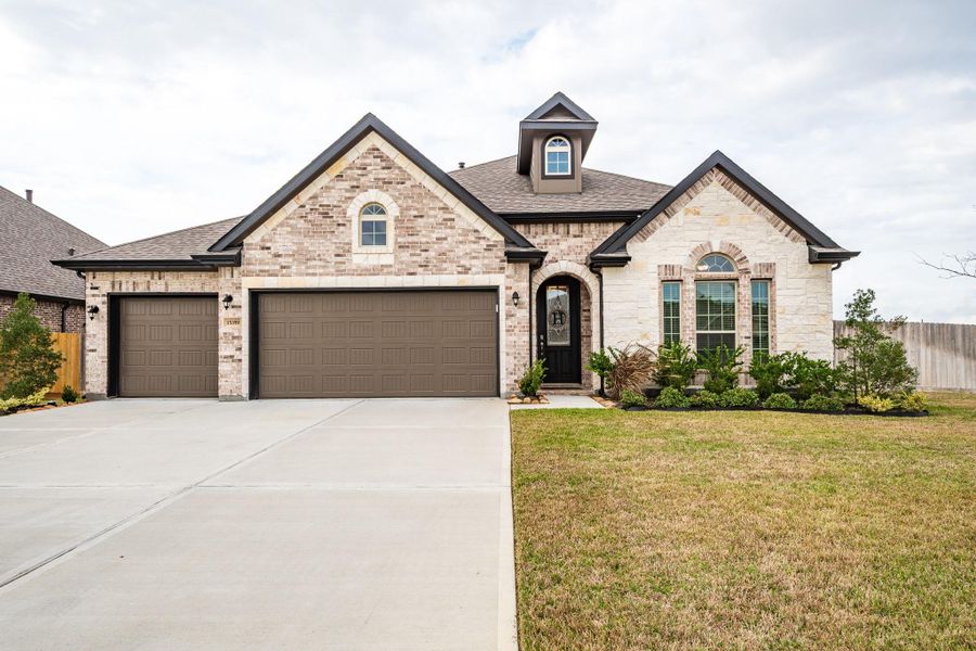 This photo showcases a modern single-story brick house with extensive stone accent, a three-car garage, and a well-maintained front lawn and garden. It features a welcoming entryway with a dark front door and decorative landscaping. This photo showcases a modern single-story brick house with extensive stone accent, a three-car garage, and a well-maintained front lawn and garden. It features a welcoming entryway with a dark front door and decorative landscaping.