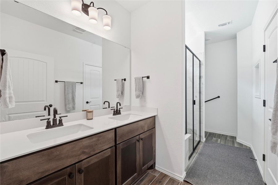 Bathroom featuring a shower stall, double vanity, and dark wood-type flooring