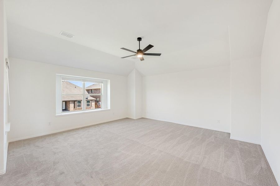 Empty bedroom with vaulted ceiling, ceiling fan, carpet flooring, and a large window Empty bedroom with vaulted ceiling, ceiling fan, carpet flooring, and a large window