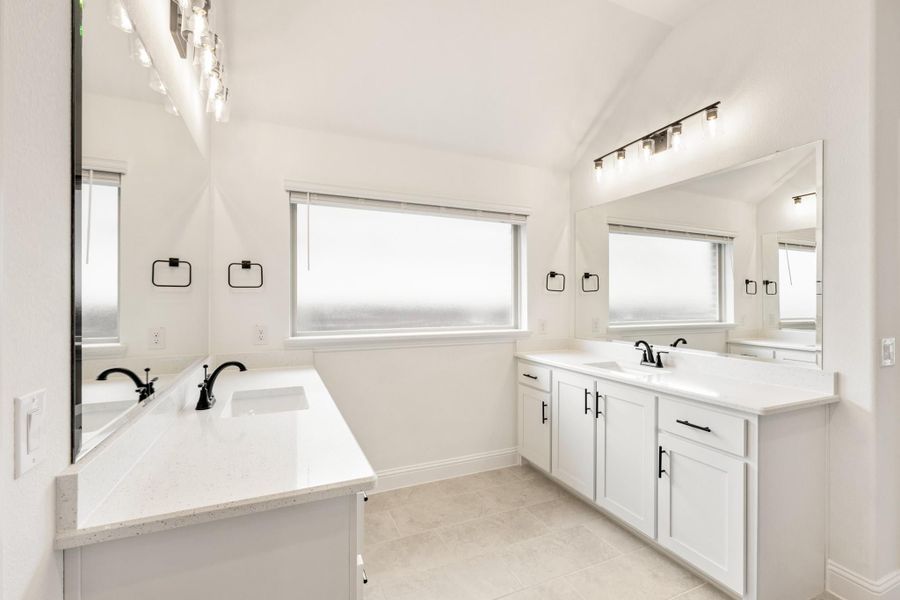 Bathroom with dual vanities, white quartz countertops, black fixtures, and large mirrors with vaulted ceiling