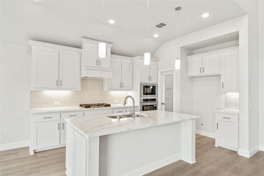 White kitchen with large island, quartz countertops, pendant lights, and stainless steel appliances White kitchen with large island, quartz countertops, pendant lights, and stainless steel appliances