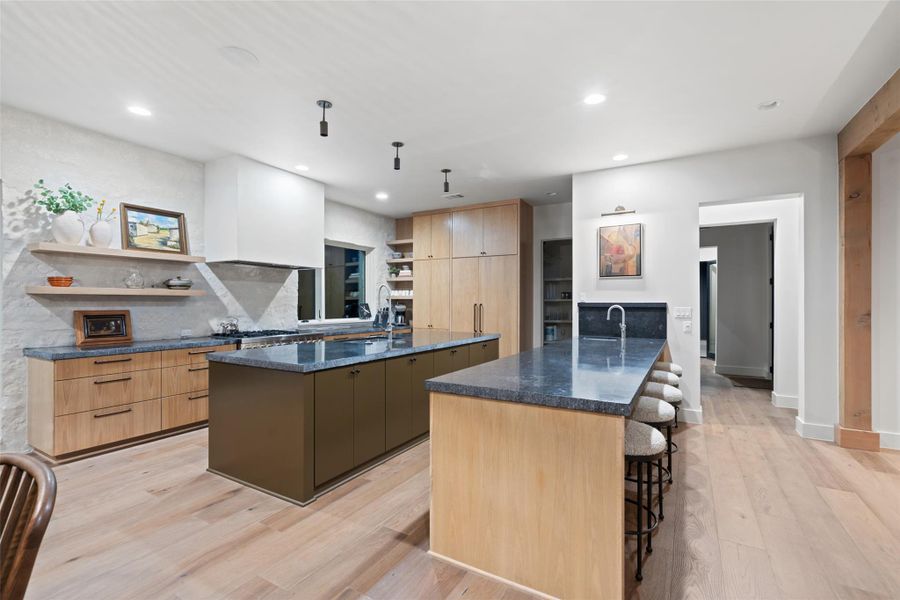 Kitchen featuring open shelves, dark stone counters, a peninsula, light wood-style floors, and a kitchen bar