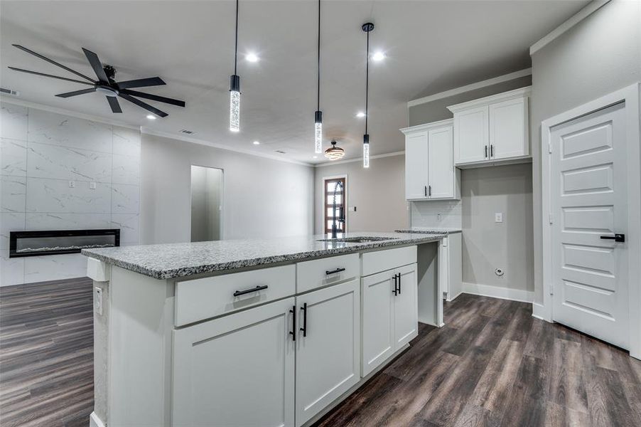 Kitchen featuring a ceiling fan, crown molding, light stone countertops, a center island, and dark wood finished floors Kitchen featuring a ceiling fan, crown molding, light stone countertops, a center island, and dark wood finished floors
