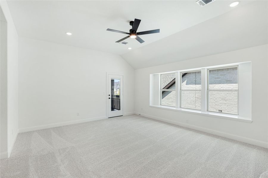 Empty room with vaulted ceiling, ceiling fan, carpet flooring, large windows, and a glass back door Empty room with vaulted ceiling, ceiling fan, carpet flooring, large windows, and a glass back door