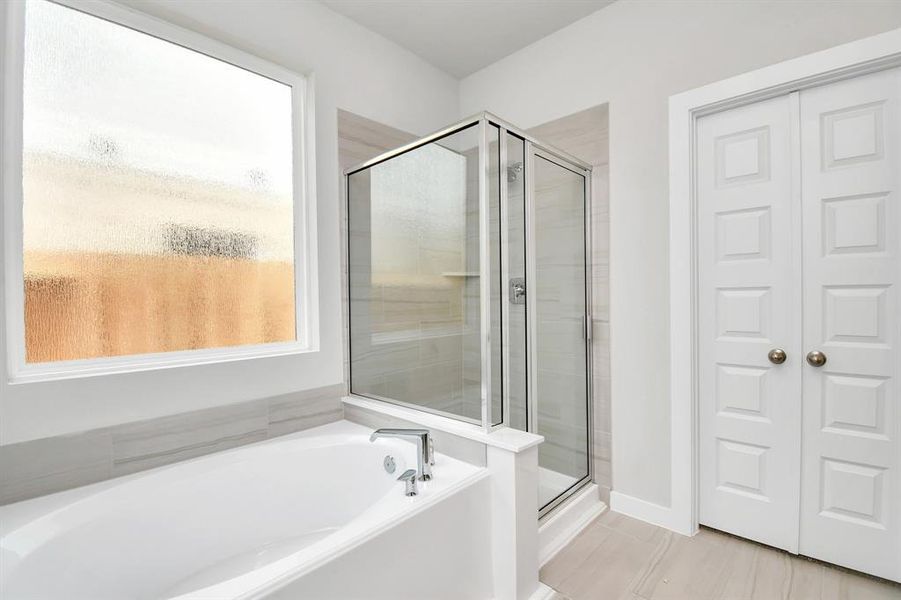 Experience a spa-like escape right in the heart of your primary bathroom. The expansive walk-in shower, surrounded by tile, and the distinctive garden tub with unique accents elevate your daily routine. The sophisticated vanity, featuring double sinks, dark-colored countertops, contemporary hardware, and bright recessed lighting, adds both style and functionality to the space. Example photo of completed home with similar plan. Actual may vary.