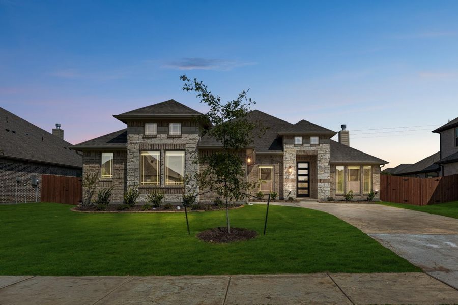 Single-story home with stone and brick exterior, large windows, and manicured front lawn at dusk