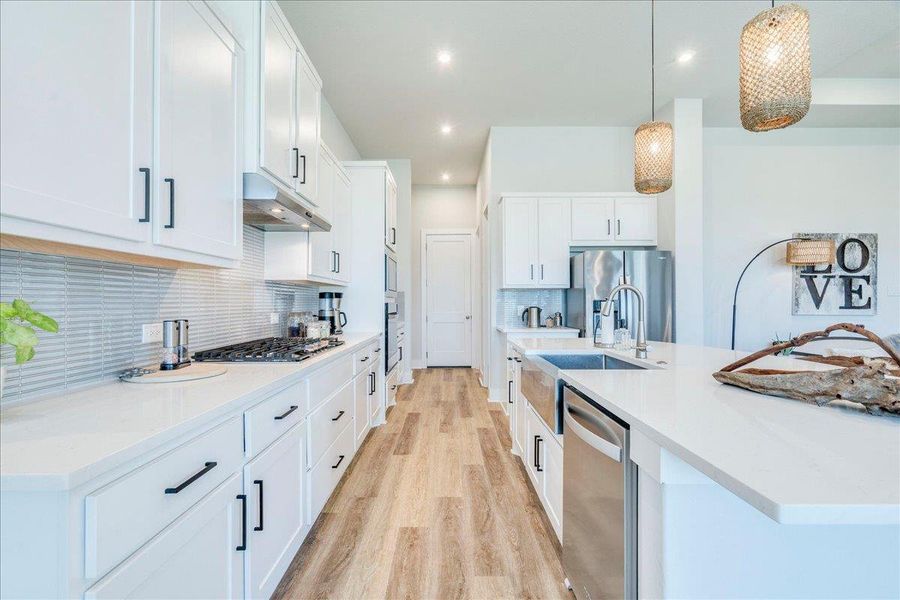 Kitchen featuring light wood finished floors, white cabinets, an island with sink, and pendant lighting Kitchen featuring light wood finished floors, white cabinets, an island with sink, and pendant lighting