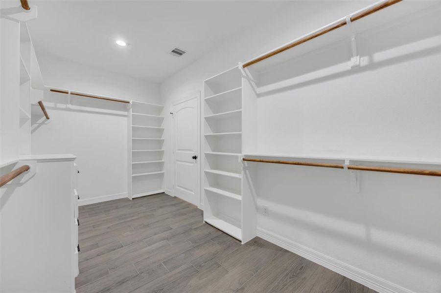 Spacious walk-in closet featuring ample shelving, hanging space, and wood-look flooring, perfect for organized storage in a modern, well-lit setting. Spacious walk-in closet featuring ample shelving, hanging space, and wood-look flooring, perfect for organized storage in a modern, well-lit setting.