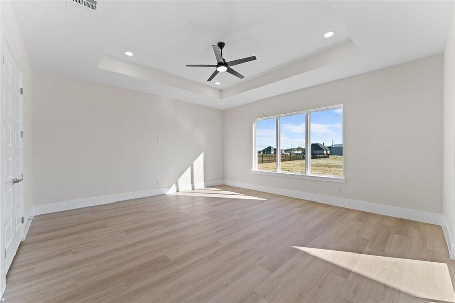 Empty room featuring a tray ceiling, light wood-style floors, ceiling fan, and recessed lighting Empty room featuring a tray ceiling, light wood-style floors, ceiling fan, and recessed lighting