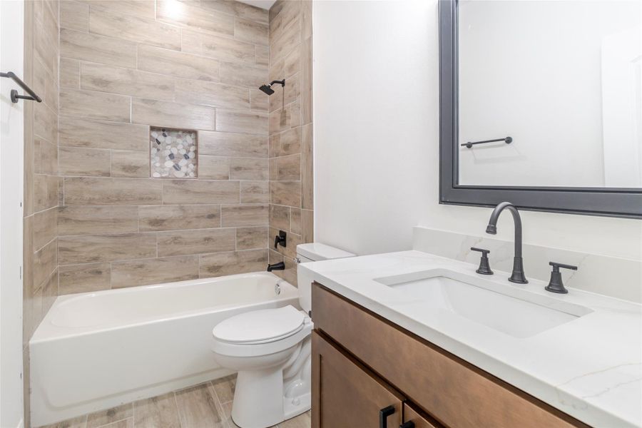 The second full bath carries through the quartz, wood cabinetry, matte-black fixtures, and tile surround. The second full bath carries through the quartz, wood cabinetry, matte-black fixtures, and tile surround.