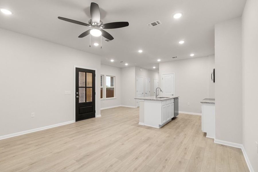 This open-concept living area features light-toned flooring, recessed lighting, and a ceiling fan