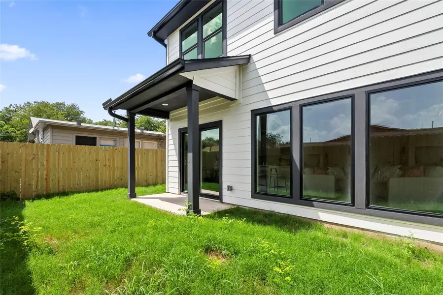 A modern facade with crisp siding and dark-framed windows overlooks a vibrant backyard, featuring a covered patio area.