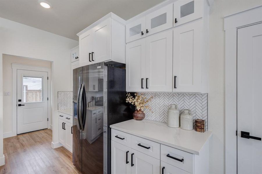 Kitchen with white cabinetry, stainless steel fridge with ice dispenser, decorative backsplash, and light hardwood / wood-style flooring Kitchen with white cabinetry, stainless steel fridge with ice dispenser, decorative backsplash, and light hardwood / wood-style flooring