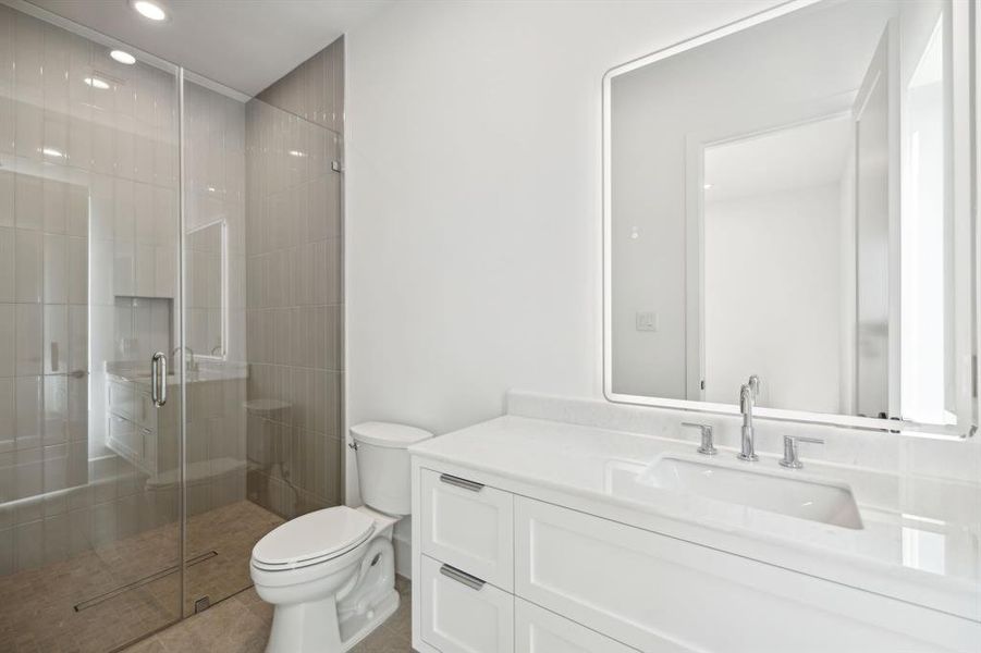 This secondary bathroom showcases a modern and minimalistic design with a soothing color palette. The vanity offers marble counters and a custom mirror.