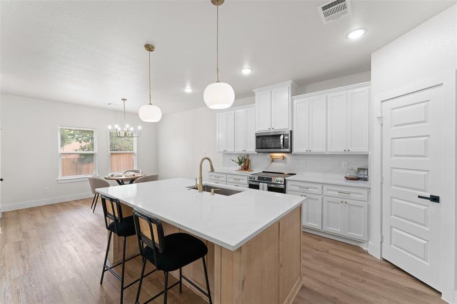 Kitchen featuring appliances with stainless steel finishes, a sink, light wood-type flooring, an island with sink, and a kitchen breakfast bar Kitchen featuring appliances with stainless steel finishes, a sink, light wood-type flooring, an island with sink, and a kitchen breakfast bar