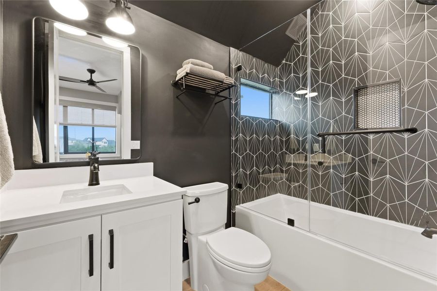 Bathroom with geometric patterned wall tile, white vanity with integrated sink, dark bronze fixtures, glass shower enclosure, and a built-in shower niche Bathroom with geometric patterned wall tile, white vanity with integrated sink, dark bronze fixtures, glass shower enclosure, and a built-in shower niche