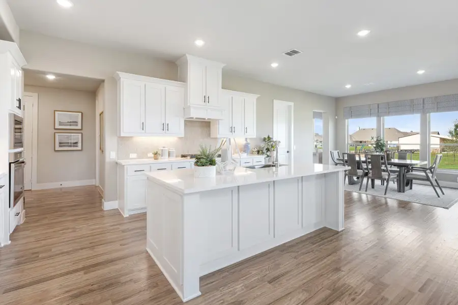 Open kitchen with white cabinets, large center island, and wood floors leading to dining area