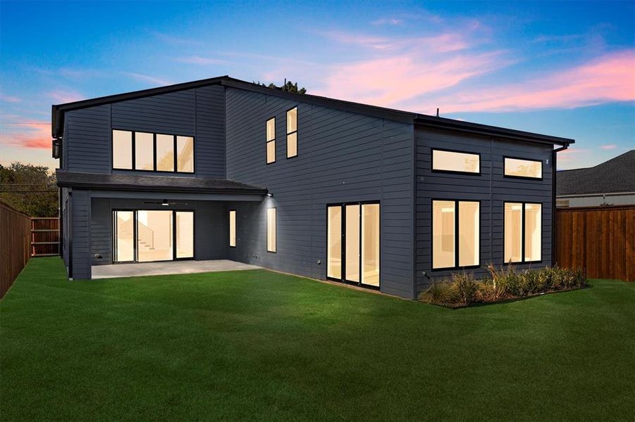 Back house at dusk with a lawn and a patio area