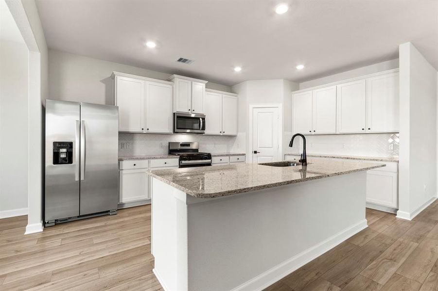 The kitchen features large island with sink and breakfast bar, beautiful white cabinetry, and stainless steel appliances.