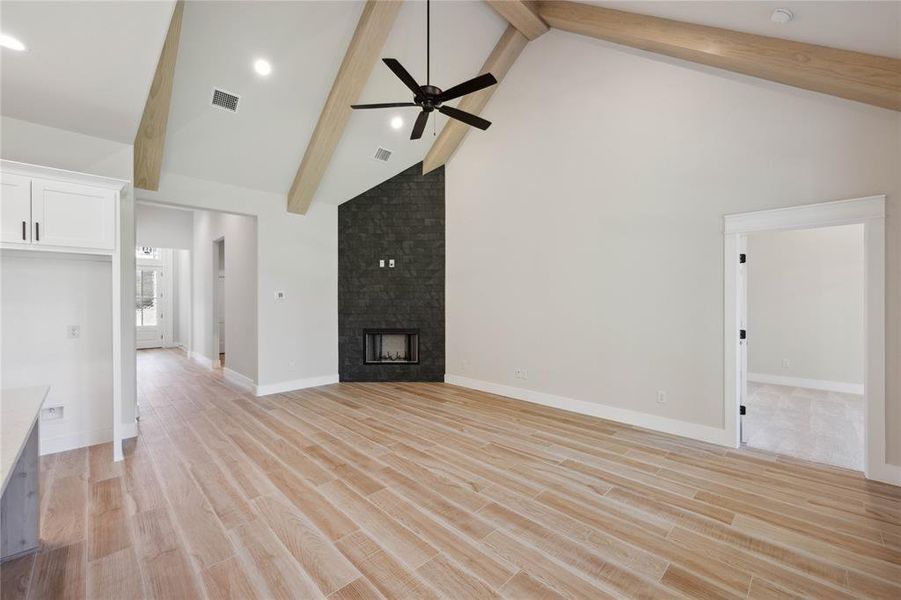 Unfurnished living room featuring beam ceiling, a fireplace, high vaulted ceiling, and light wood-type flooring