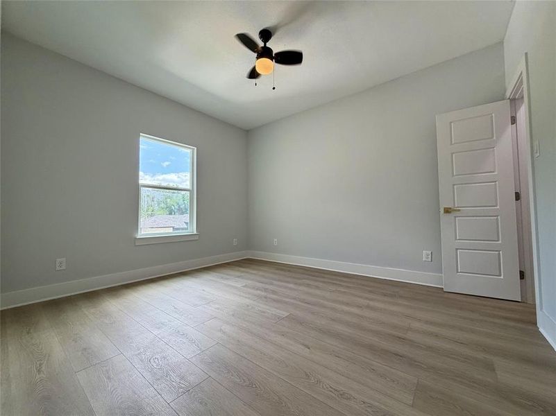 Spacious room featuring wood-finish flooring, a contemporary ceiling fan with integrated lighting, a multi-pane window, and a modern five-panel interior door Spacious room featuring wood-finish flooring, a contemporary ceiling fan with integrated lighting, a multi-pane window, and a modern five-panel interior door