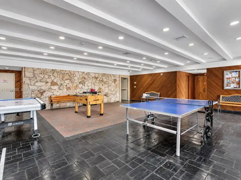 Textured natural stone accent wall, wood-paneled wall detailing, dark slate tile flooring, and recessed ceiling lighting with exposed beam accents