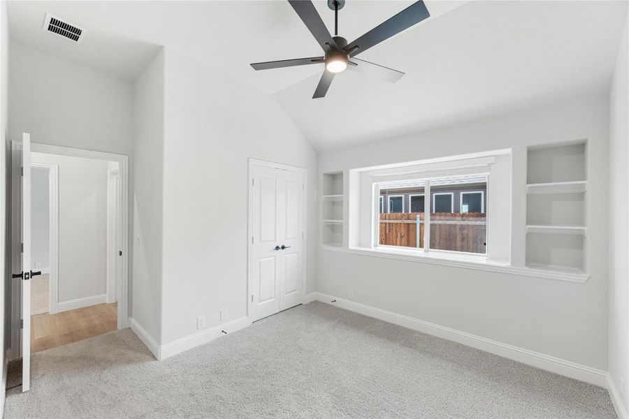 Bedroom with vaulted ceiling, ceiling fan, built-in shelves, and carpet flooring