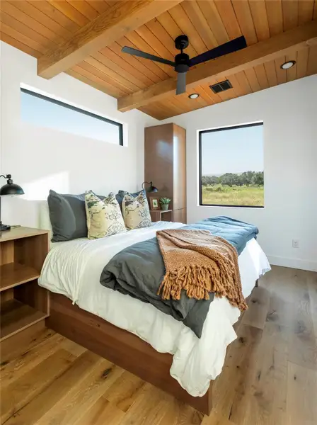 Serene master bedroom retreat with warm wood ceilings, large picture windows, and calming Hill Country views.